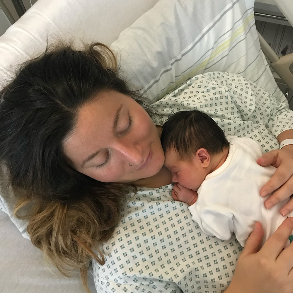 Woman in her 30s holding her baby in the hospital after an emergency C-section, representing empowerment and overcoming irrational fear of C-section.
